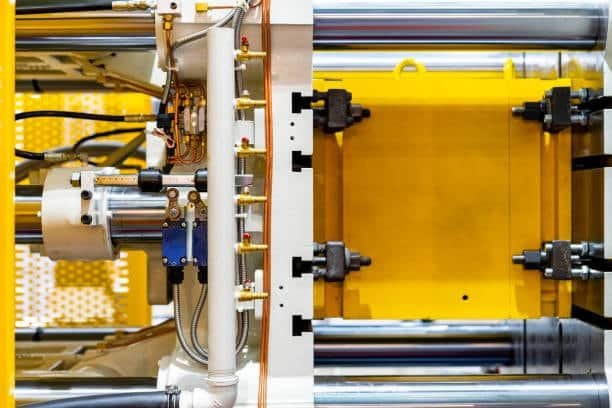 Open mold setup inside an injection molding machine using a cold runner system with a yellow mold base.