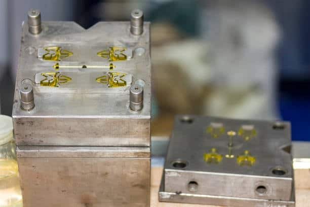 Injection mold using a hot runner system with multiple cavities and yellow molded components.