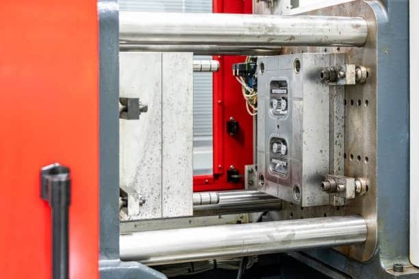 Metal mold installed inside an injection molding machine with red protective housing.