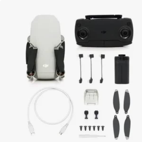 Folded white foldable drone alongside its black remote controller, battery, propellers, USB cable, and accessory connectors laid out on a white surface.