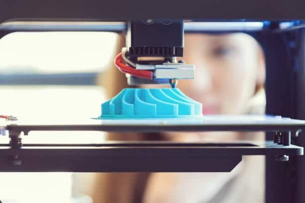 A blue prototype of an impeller or turbine blade being printed using additive manufacturing.