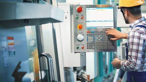Male engineer interacting with CNC controller to input machining program on a factory floor