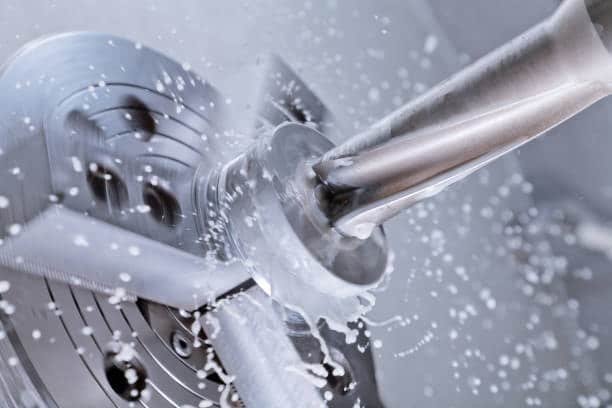 Metal workpiece being cut on CNC machine with coolant spraying for temperature and chip control
