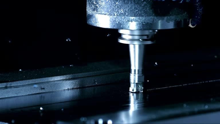 Close-up of vertical CNC mill cutting metal sheet using programmed path in a dark environment