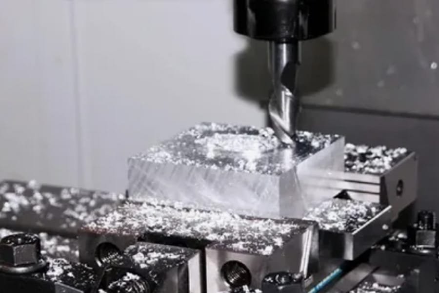 CNC milling machine cutting a rectangular aluminum block with chips around, demonstrating multi-axis machining in progress.