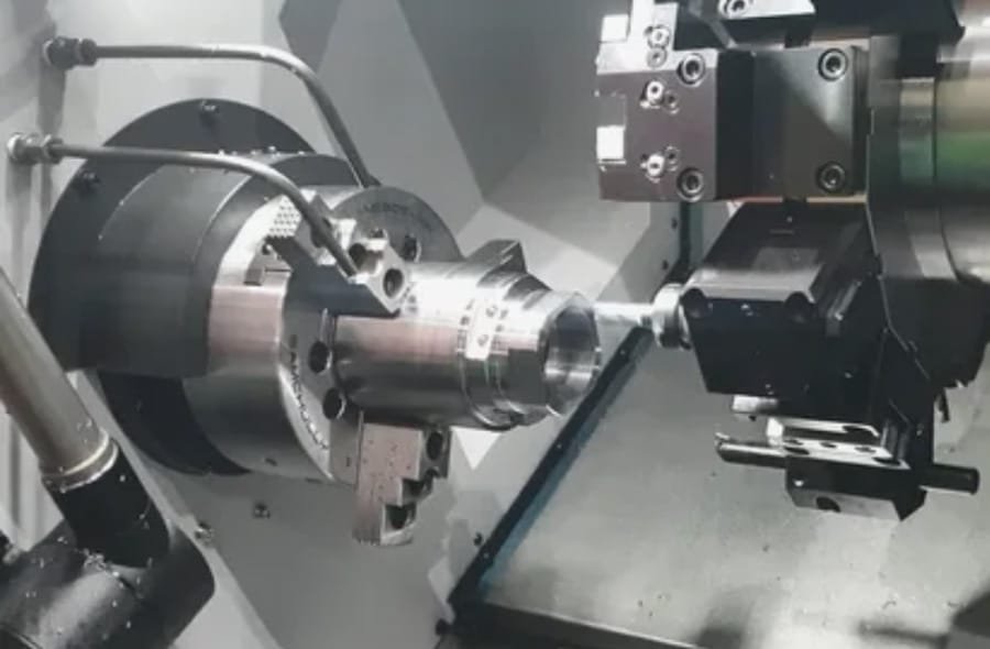 CNC lathe turning a cylindrical metal workpiece with a live-tool spindle, showcasing precision machining of a complex metal component.