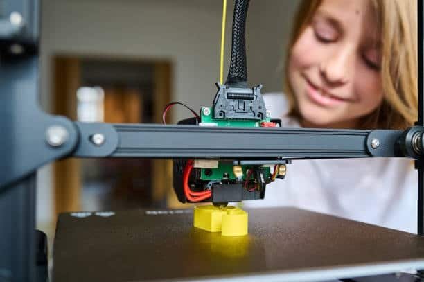 Young person observing 3D printer producing yellow mold part