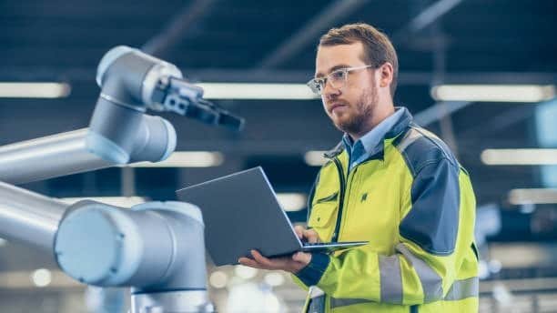 Technician in high-vis jacket analyzing CNC robotic system using real-time software interface