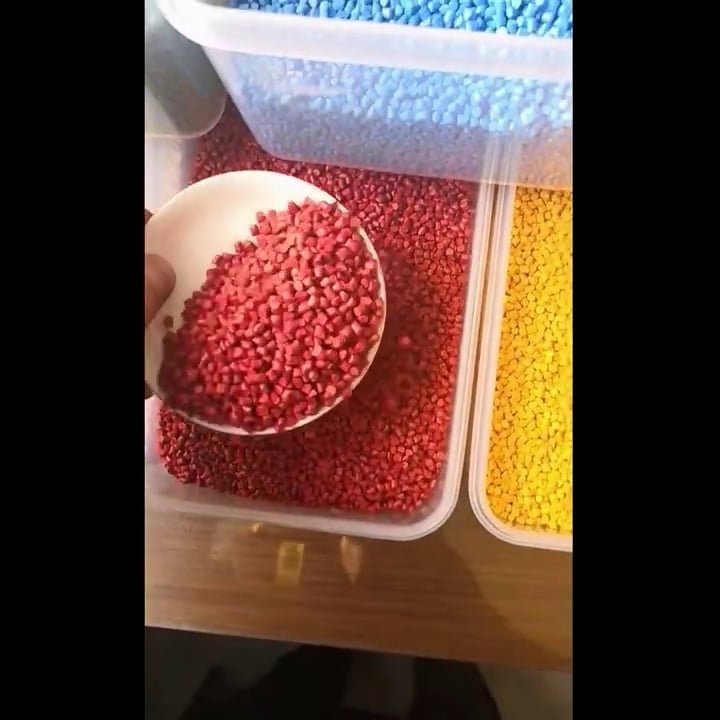 Red polypropylene granules being scooped from large storage bins in a manufacturing facility
