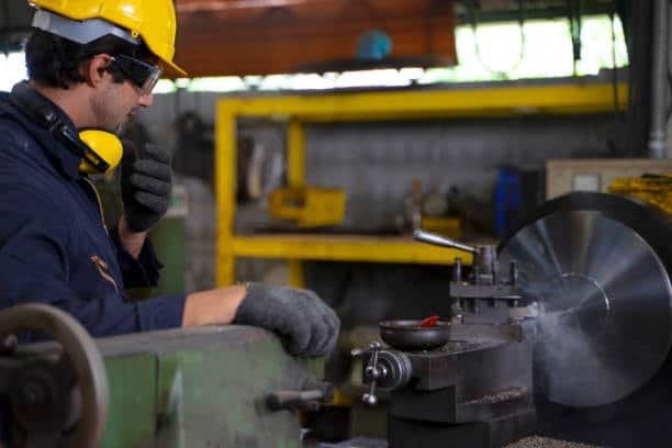 Lathe operator wearing safety gear closely watching a metal turning operation where chatter may occur