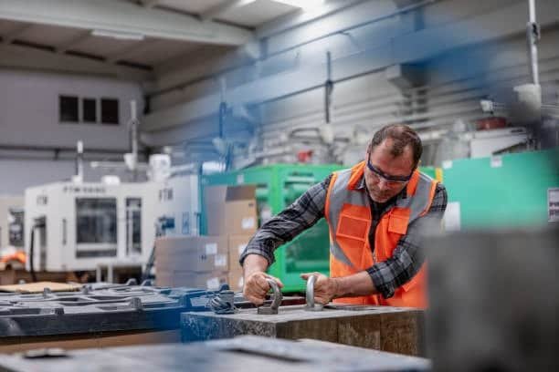 Worker inspecting and adjusting metal molds in an injection molding facility
