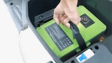 Hand placing a green electric vehicle battery pack into a vehicle compartment, illustrating advanced battery technology in action.