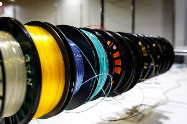 Various PLA filament spools with vibrant colors on industrial display rod
