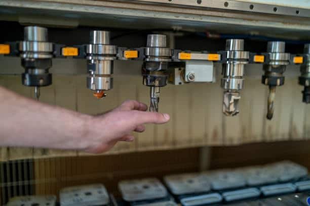 Image of a hand adjusting a cutting tool among several mounted tools on a CNC machine, with additional tools and equipment stored below.