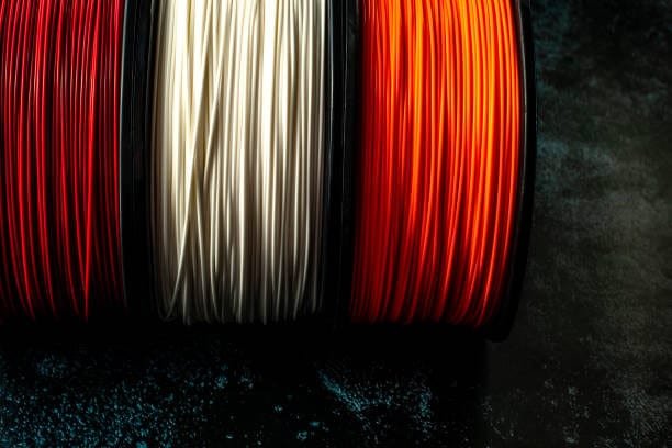 Side view of white green and red PLA spools on black background