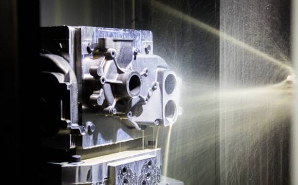Precision-machined part clamped in CNC setup, sprayed with coolant, under inspection for chatter-related surface defects
