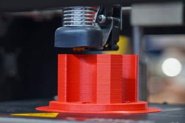 Red mechanical mold part in progress on FDM 3D printer bed