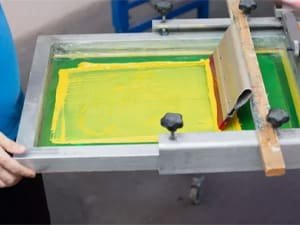 Technician performing pad printing on an injection molded plastic part using a screen and squeegee.