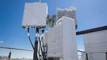 Outdoor 5G base station enclosure units mounted on a rooftop, showing RF module housings and protective covers with connecting cables.