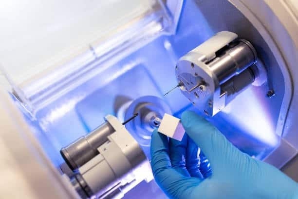 Gloved hand loading a square ABS plastic block into dental CNC milling machine for fabrication