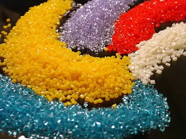Yellow, red, purple, white, and blue ABS plastic granules arranged in a curve, symbolizing vibrant, safe materials.