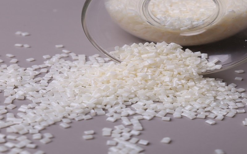 White ASA plastic pellets spilling from a container for molding.