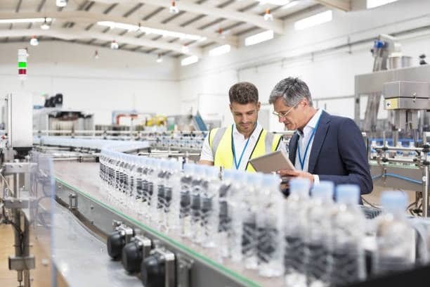 Quality inspectors reviewing output on a plastic bottle filling and packaging line for defects and consistency