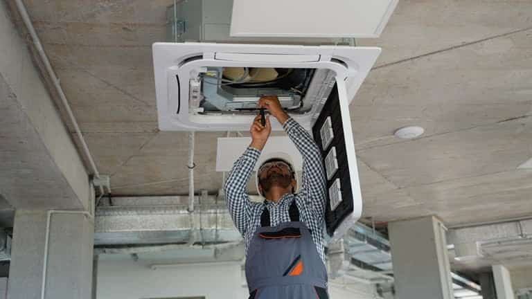 Technician installing a ceiling-mounted HVAC unit with integrated fixture system
