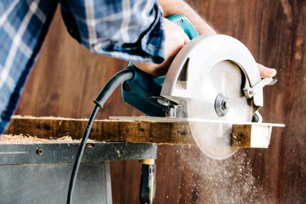 Manual circular saw in action cutting a wood board, showcasing sawdust and precision grip