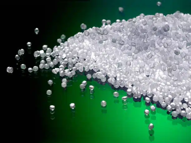 FDA-grade clear ABS plastic granules on a green surface, used for safe consumer product manufacturing.