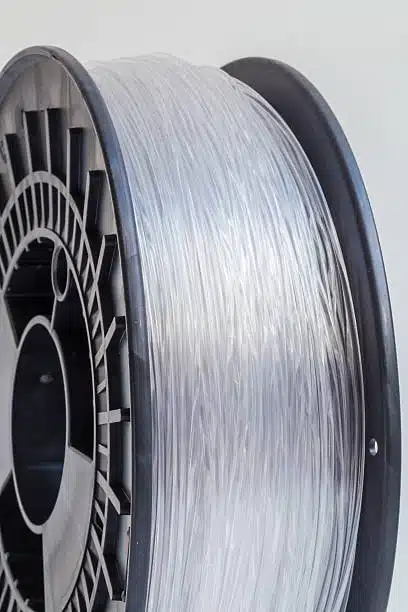 Transparent polycarbonate filament wound on a spool, showing rigidity and optical clarity.
