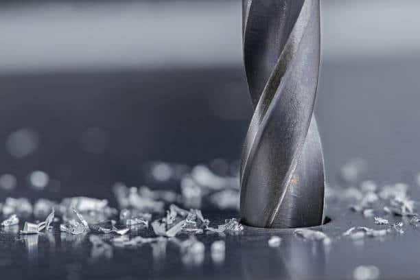 Drill bit in the middle of drilling a hole on a metal surface with debris