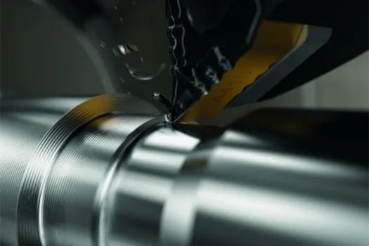 CNC lathe performing a live-tooling cut on a cylindrical metal workpiece to achieve tight tolerances and complex profiles.