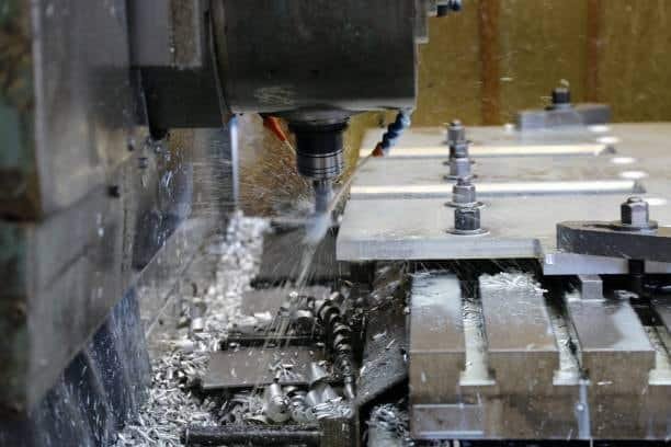 CNC machine cutting aluminum plate while coolant sprays metal chips