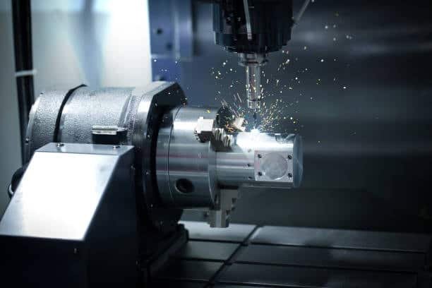 CNC milling machine cutting a square metal block with sparks during the process
