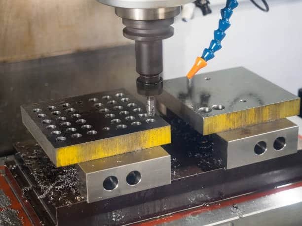 CNC milling machine working on a fixtured metal block with drilling operations in progress