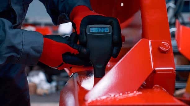 Operator checking coating thickness for surface tolerance on painted metal part