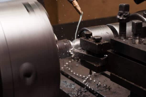 Lathe tool cutting cylindrical metal workpiece with fluid coolant