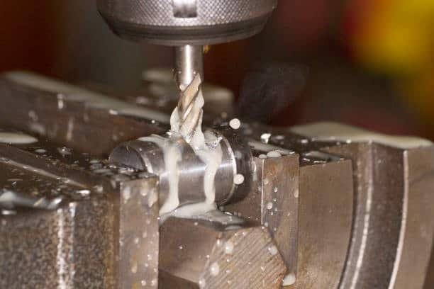 End mill machining a cylindrical metal piece with cutting fluid