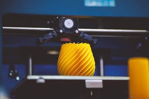 3D printer creating a yellow spiral decorative object using FDM extrusion technology.