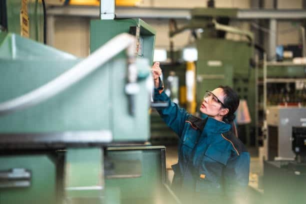 Woman inspecting operational status of CNC equipment during quality control round in manufacturing environment