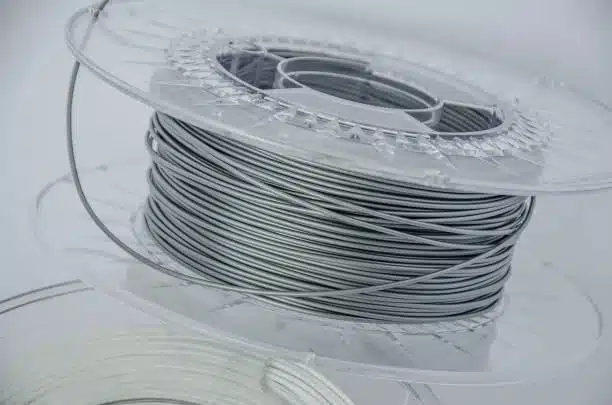 Gray polycarbonate filament on a transparent reel, suitable for industrial 3D printing.