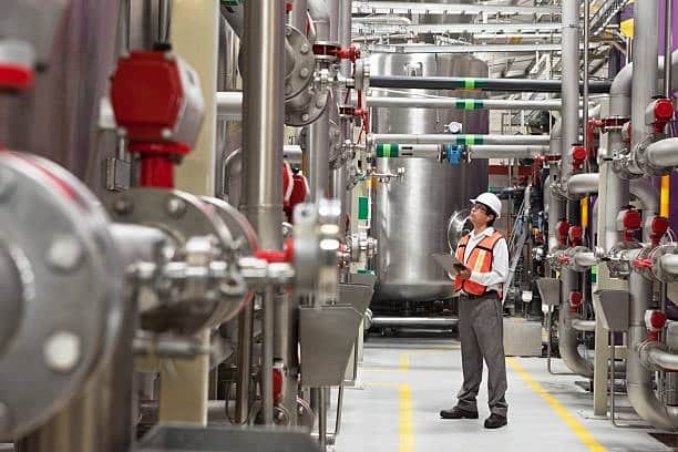 Industrial quality control engineer conducting inspection rounds among automated process equipment and tanks