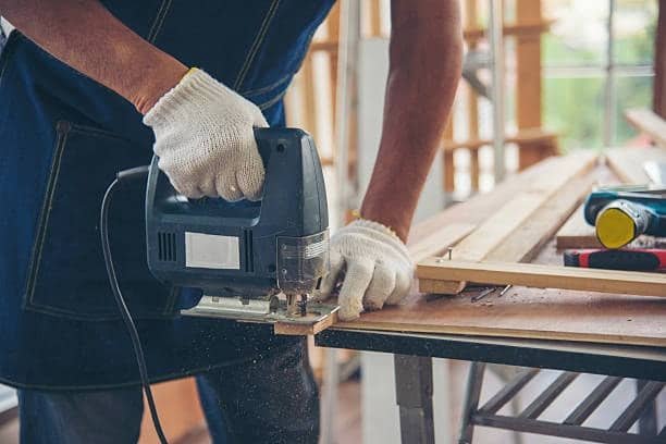 Close-up of a person using a jigsaw to cut through plywood on a workbench