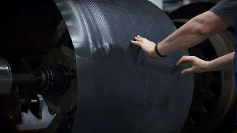 Technician aligning a large sheet of carbon fiber material on an industrial roller