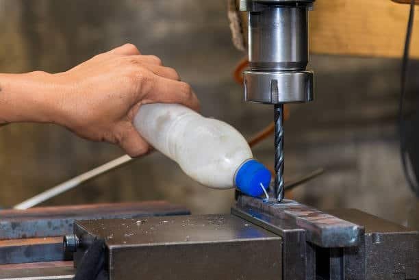 Hand applying cutting fluid directly on drill bit during manual metal drilling