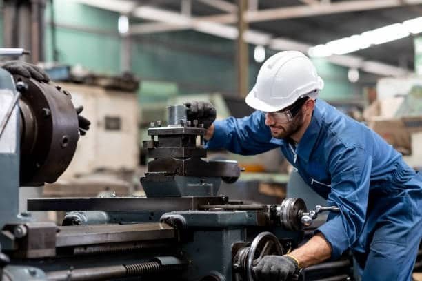 Worker setting up a manual lathe machine for custom metal part production