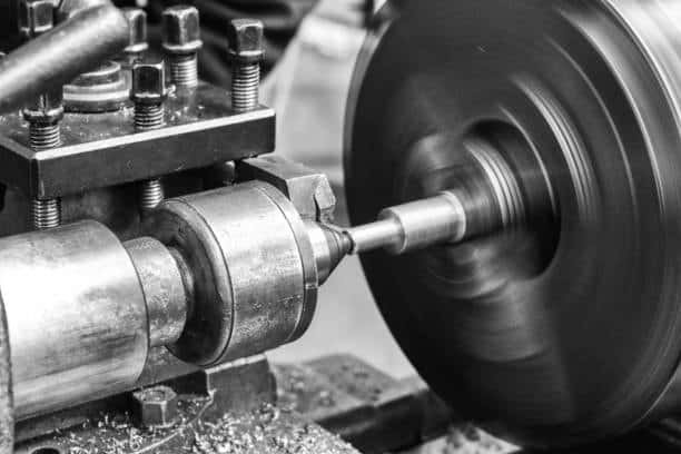 Cylindrical metal part being turned on a manual lathe with rotating spindle
