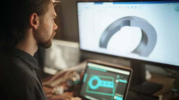 Mechanical engineer analyzing part performance with CAE design on dual monitors.