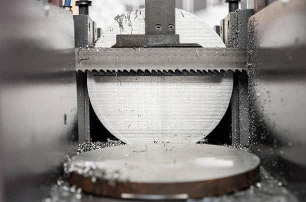 Industrial saw slicing through a thick aluminum disc with metal shavings around